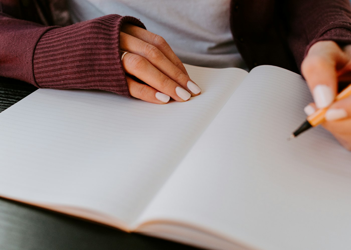 Close-up of hands holding open a lined notebook and writing with a pencil.